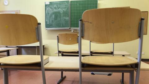 Hochgestellte Stühle im Klassenraum einer Schule. Im Hintergrund ist eine Tafel zu sehen.