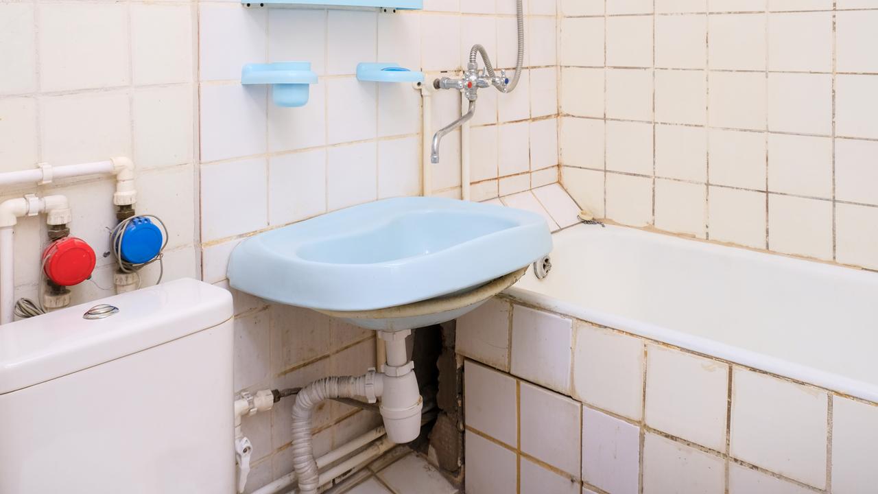 In einem altmodischen Badezimmer hängt ein blaues Waschbecken und steht eine eingemauerte Badewanne.