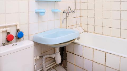 In einem altmodischen Badezimmer hängt ein blaues Waschbecken und steht eine eingemauerte Badewanne.