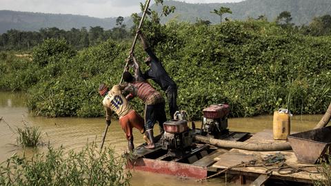 Eine Gruppe illegaler Goldwäscher benutzt eine motorisierte Pumpe, um das Flussbett auf der Suche nach Goldstücken zu durchwühlen. Region Kibi im Süden Ghanas, 2017. 