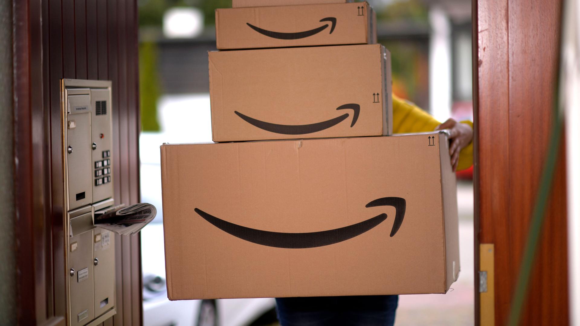 Ein Lieferbote liefert mehrere Pakete von Amazon an einer Haustür ab.