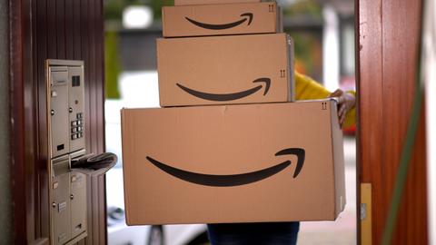 Ein Lieferbote liefert mehrere Pakete von Amazon an einer Haustür ab.