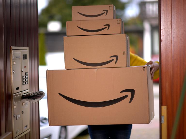 Ein Lieferbote liefert mehrere Pakete von Amazon an einer Haustür ab.