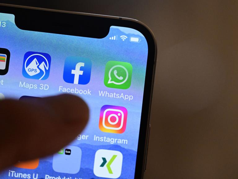 Eine Hand hält ein iPhone, auf dem Social Media Apps dargestellt sind (gestellte Szene).