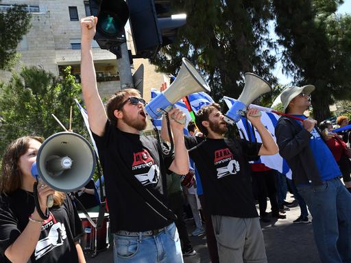 Aktivisten protestieren auf der Straße: Sie recken die Faust nach oben, rufen in Megaphone und tragen T-Shirts mit politischen Slogans.