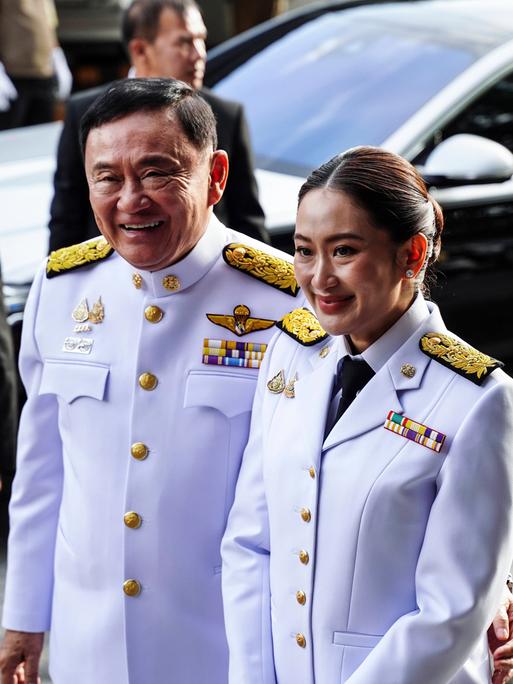 Paetongtarn Shinawatra mit ihrem Vater Thaksin Shinawatra. Beide tragen weisse Uniformen.
