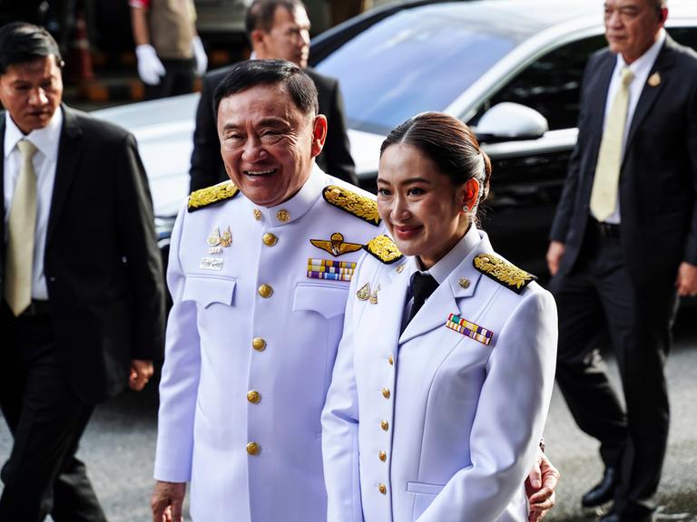 Paetongtarn Shinawatra mit ihrem Vater Thaksin Shinawatra. Beide tragen weisse Uniformen.
