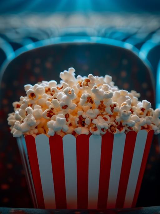Bucket of popcorn sitting on seat in empty movie theater,  03.07.2024, Copyright: xalphaspiritx Panthermedia37544096.jpg 
