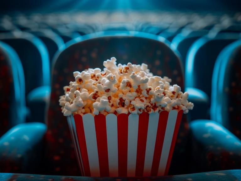 Bucket of popcorn sitting on seat in empty movie theater,  03.07.2024, Copyright: xalphaspiritx Panthermedia37544096.jpg 