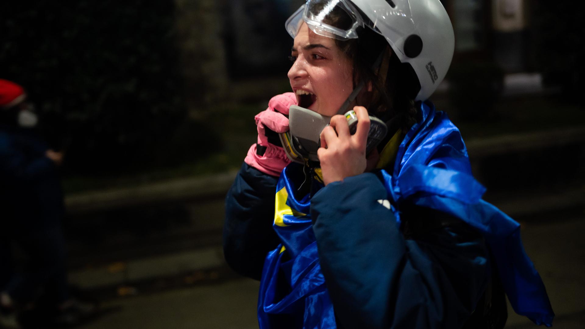 Eine Frau mit Helm und blauer Flagge um den Körper scheint auf der Straße ihre Wut rauszuschreien