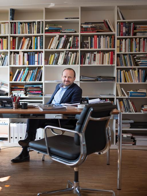 Porträt von Daniel Kampa an seinem Schreibtisch vor einem gut gefüllten Bücherregal.