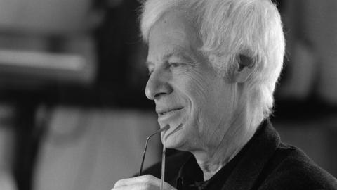 Auf dem schwarz/weiß Bild schaut ein grauhaariger Mann mit einer Brille in der Hand lächelnd zur Seite. Auf dem schwarz/weiß Bild schaut ein grauhaariger Mann mit einer Brille in der Hand lächelnd zur Seite.