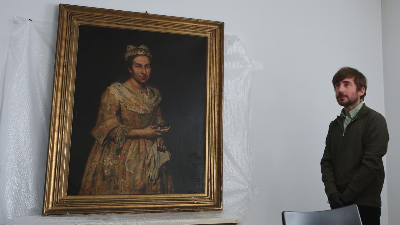 Giacomo Cerutis Gemälde "Porträt einer Dame" aus dem 18. Jahrhundert hängt an einer weißen Wand. Zwischen Bild und Wand ist Plastikfolie. Neben dem Bild steht ein Mann mit Bart. 