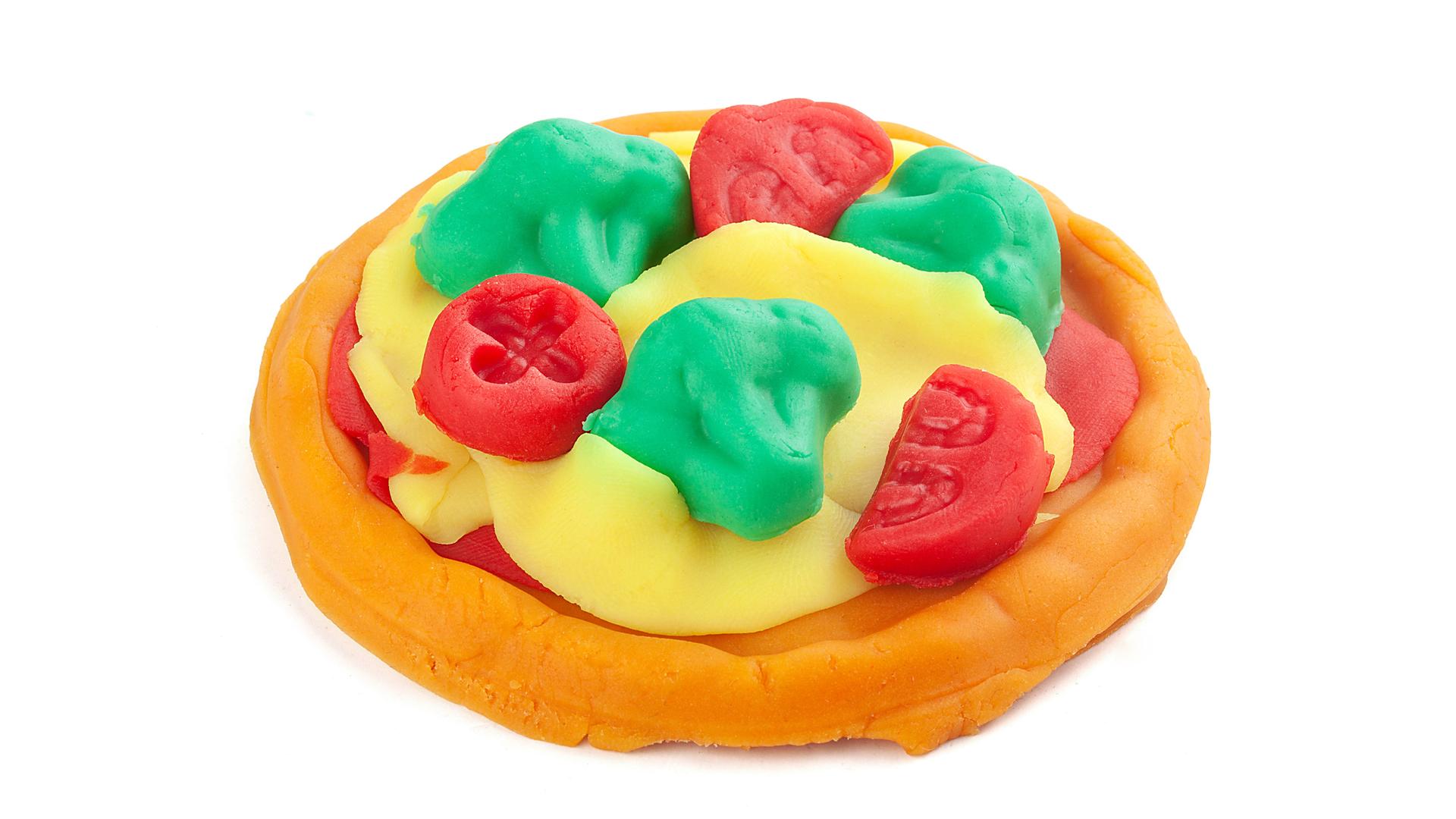 Eine aus Knete modellierte Pizza vor weißem Hintergrund mit Käse, Tomaten und Basilikum.