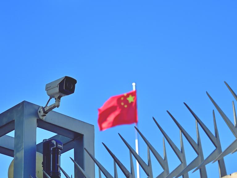 Symbolbild "China" Kamera am Zaun des Chinesischen Generalkonsulats in Frankfurt am Main, im Hintergrund weht die Flagge der Volksrepublik China.