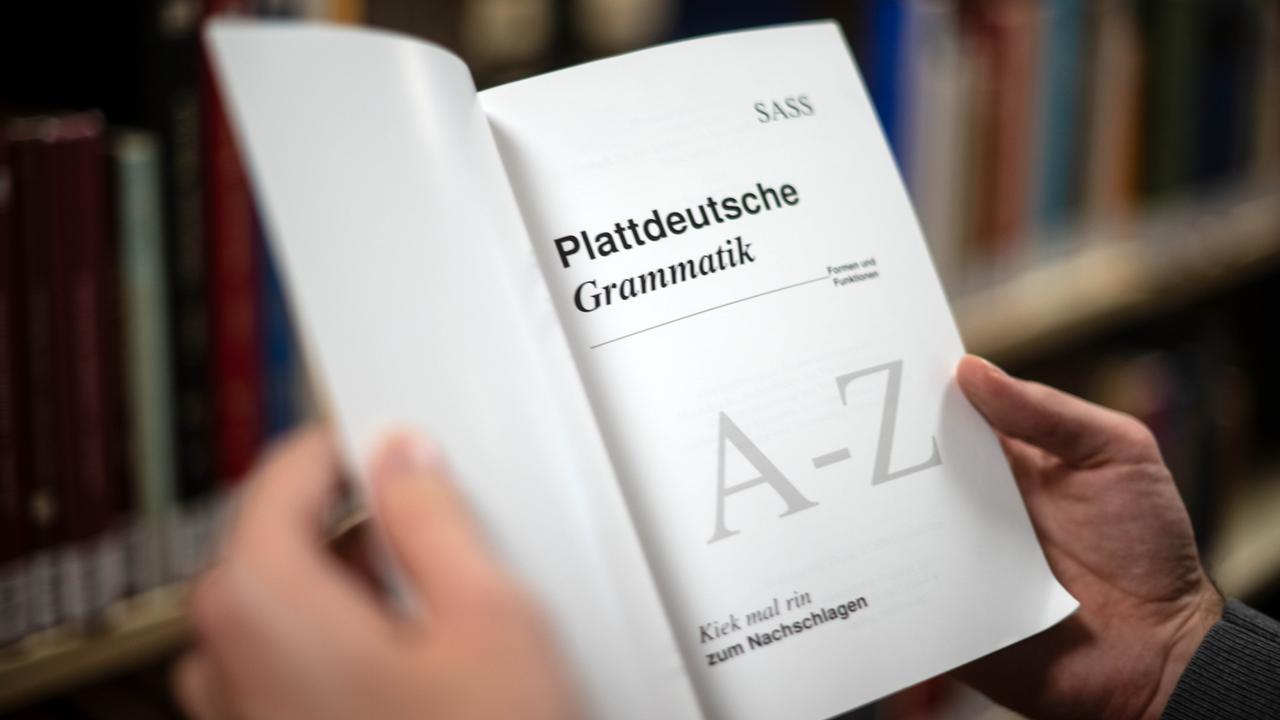 Ein Lehrbuch für die Plattdeutsche Grammatik - das Buch wird von zwei Männerhänden gehalten. 