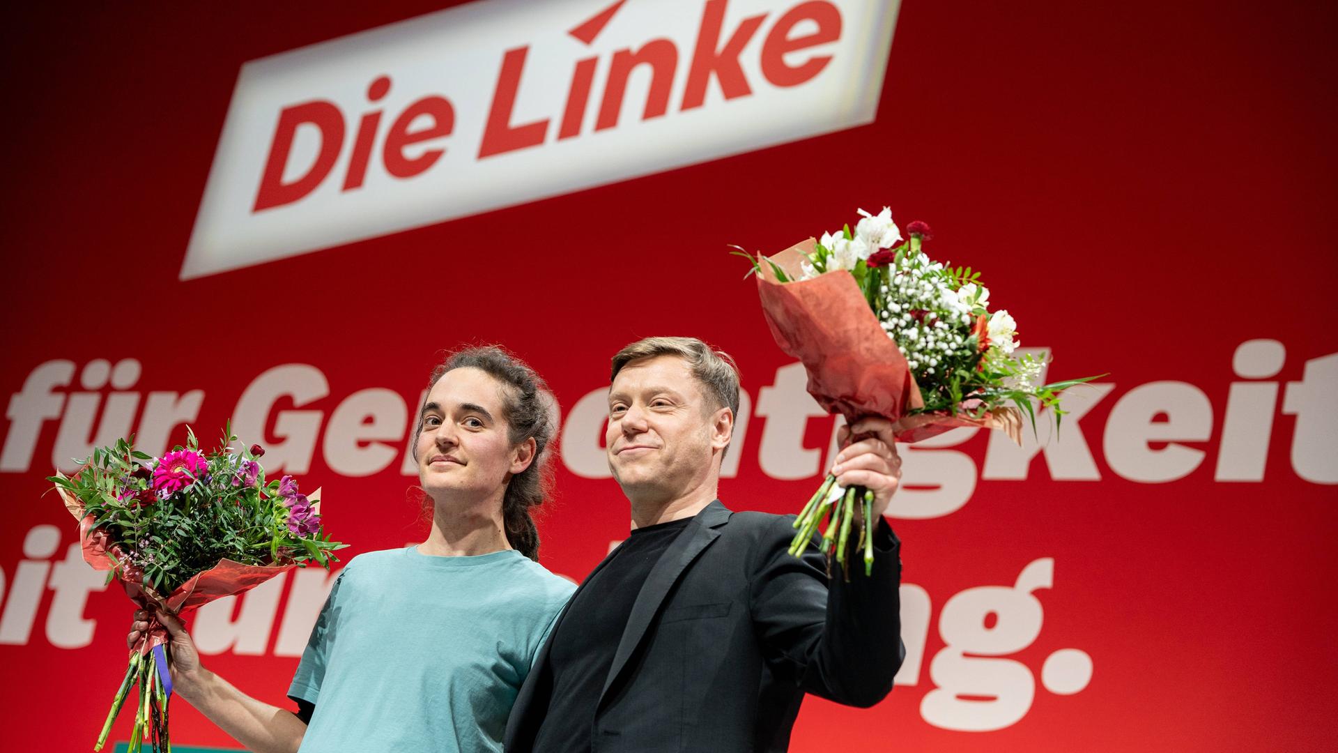 Seenotretterin Carola Rackete und Linken-Vorsitzender Martin Schirdewan stehen nebeneinander vor einer roten Wand mit "Die Linke"-Schriftzug. Sie haben jeweils einen Blumenstrauß in der Hand.