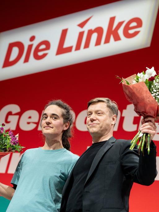 Seenotretterin Carola Rackete und Linken-Vorsitzender Martin Schirdewan stehen nebeneinander vor einer roten Wand mit "Die Linke"-Schriftzug. Sie haben jeweils einen Blumenstrauß in der Hand.