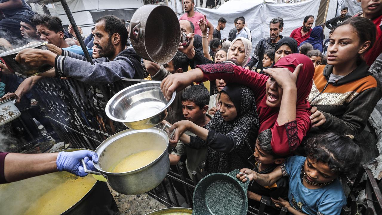 Männer, Frauen und Kinder drängen sich mit ausgestreckten Händen und Containern, um warme Mahlzeiten zu erhalten, die von Hilfsorganisationen verteilt werden.