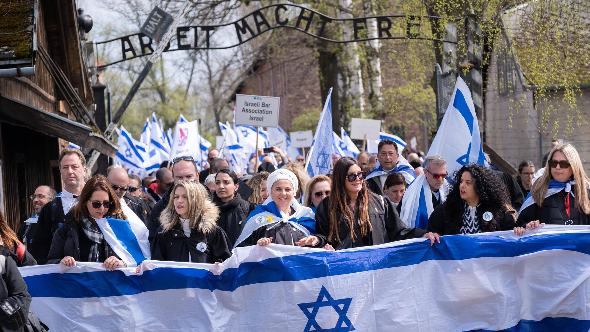 Eine Menschengruppe, teilweise mit Israel-Flaggen, läuft unter dem Schild "Arbeit macht frei" im Konzentrationslager Auschwitz hindurch.