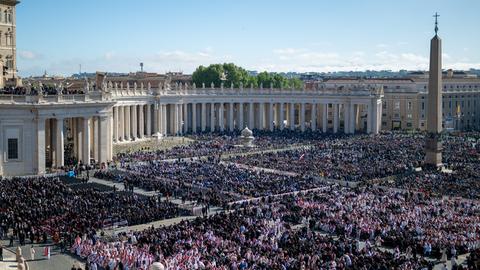 Das Bild zeigt eine Luftaufnahme des Petersplatzes, auf dem zehntausende Gläubige zur Trauerfeier für den verstorbenen Papst Franziskus zusammengekommen sind. 