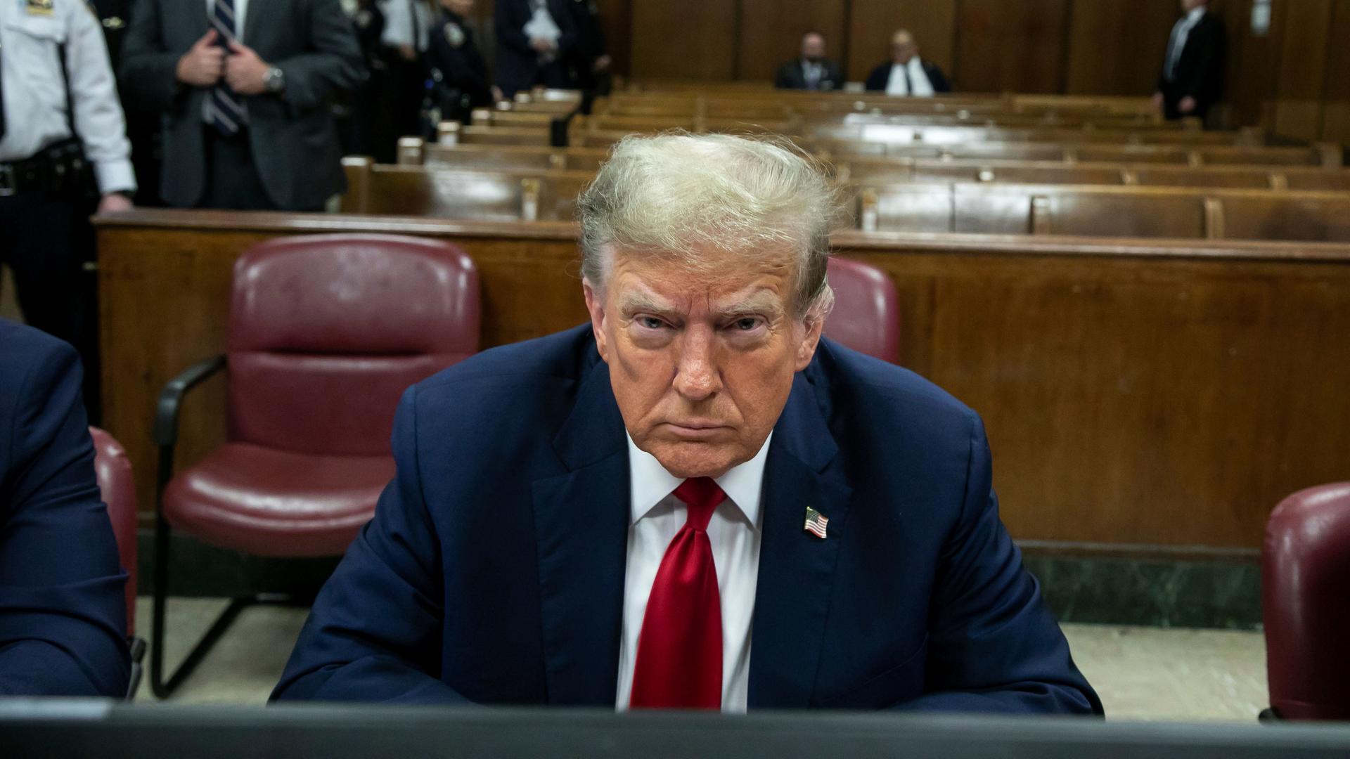Der ehemalige US-Präsident Donald Trump sitzt in einem Gerichtssaal und blickt finster in die Kamera. 