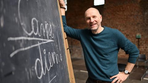Schauspieler Götz Schubert (Keating im "Club der toten Dichter) steht in der Bad Hersfelder Stiftsruine vor einer Tafel mit der Aufschrift "Carpe diem!". 