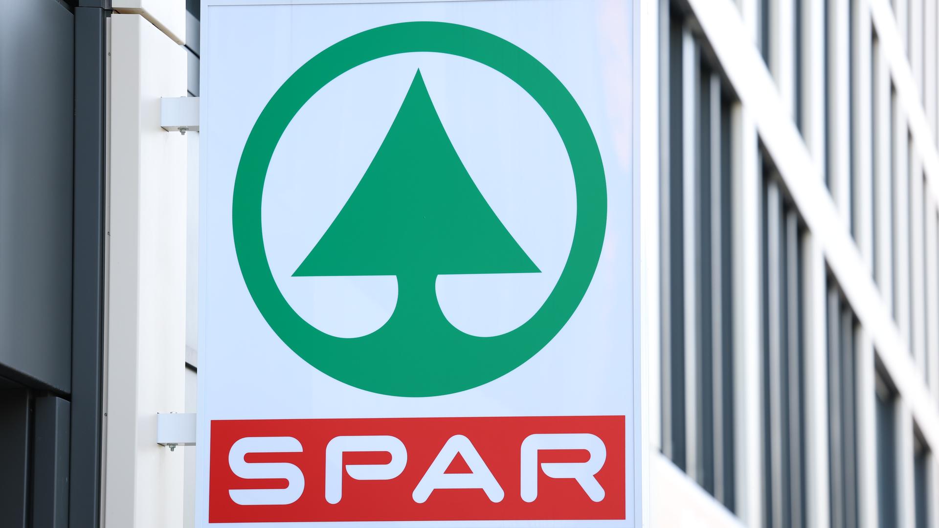Das Schild einer Spar-Filiale an einem Haus in Österreich. "Spar" ist rot geschrieben. darüber ist ein grüner stilisierter Tannenbaum.