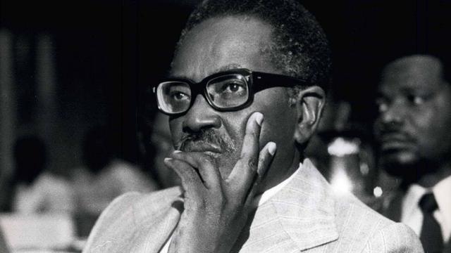 Ein Schwarz-weiß-Foto von Agostinho Neto mit schwarzer dicker Brille. Er schaut nachdenklich aus dem Bild. Ein Schwarz-weiß-Foto von Agostinho Neto mit schwarzer dicker Brille. Er schaut nachdenklich aus dem Bild.