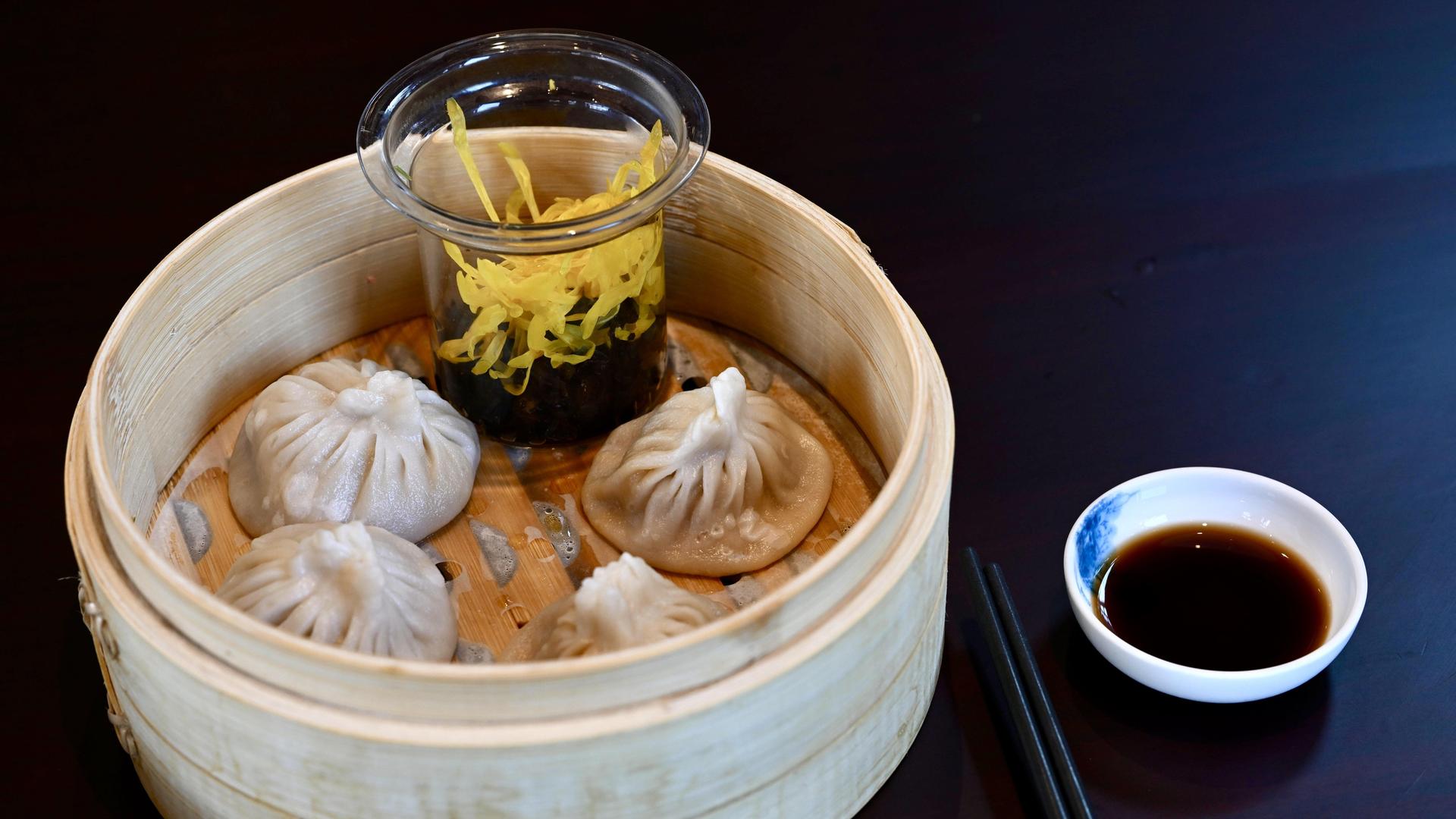 Chinesische Teigtaschen, serviert in einem Holzkörbchen, daneben Essstäbchen und Sojasoße. Chinesische Teigtaschen, serviert in einem Holzkörbchen, daneben Essstäbchen und Sojasoße.