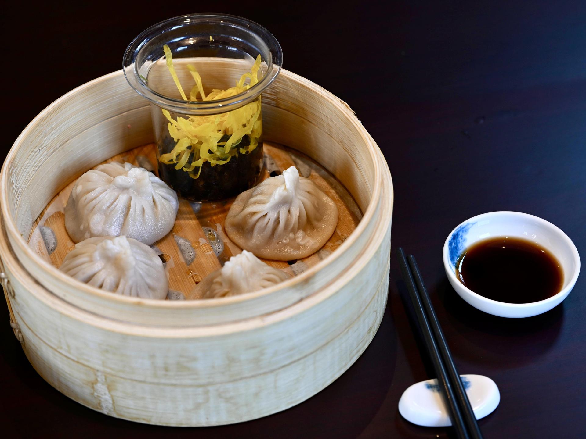 Chinesische Teigtaschen, serviert in einem Holzkörbchen, daneben Essstäbchen und Sojasoße.