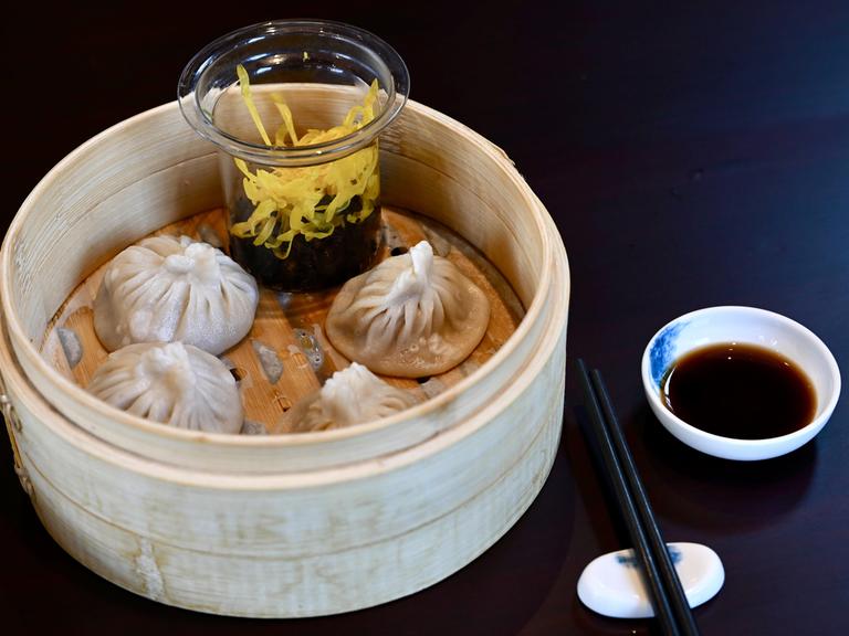 Chinesische Teigtaschen, serviert in einem Holzkörbchen, daneben Essstäbchen und Sojasoße.