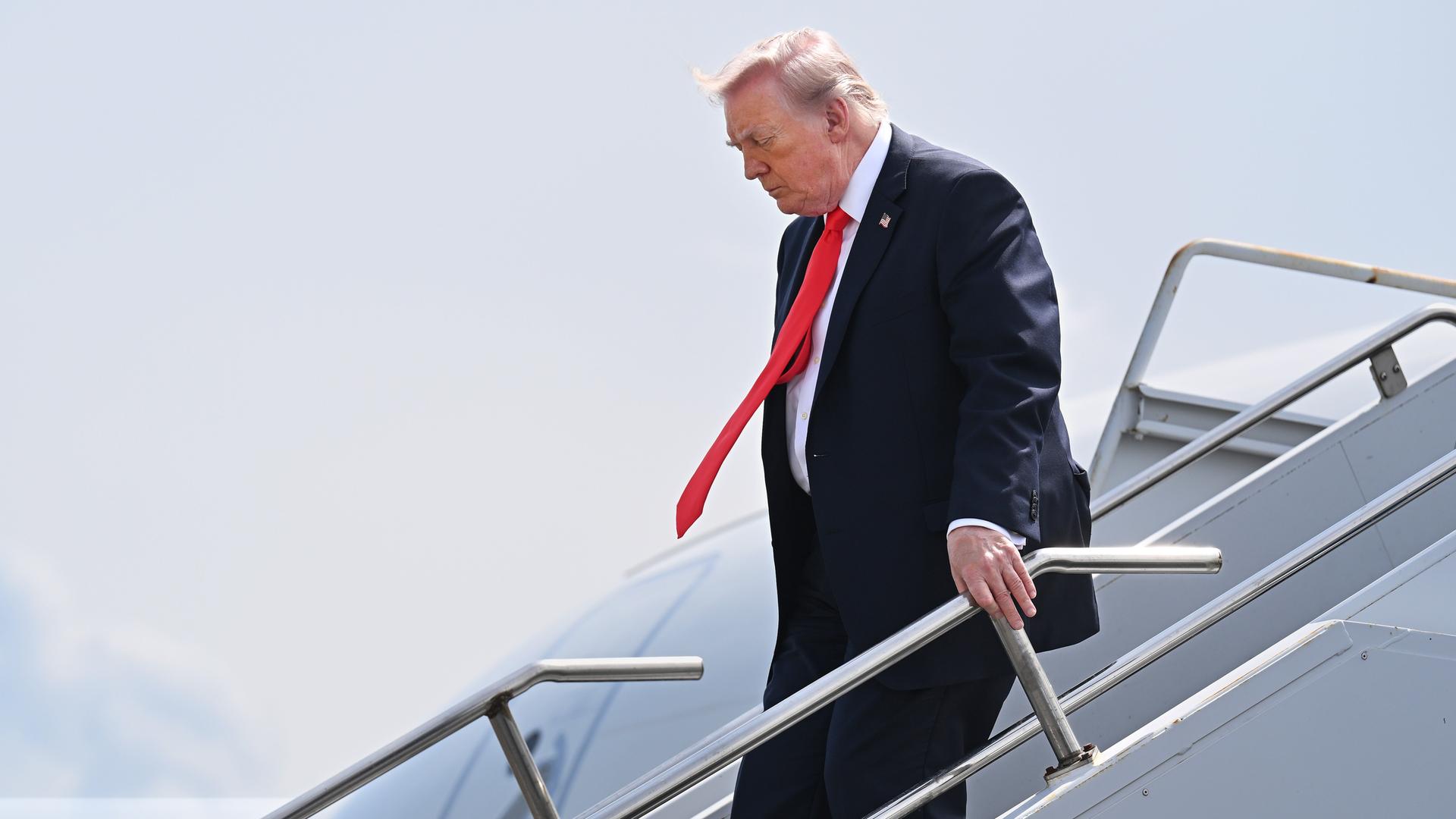 US-Präsident Donald Trump trifft am 1. Mai 2026 auf einem Flughafen in Florida, ein. Er hält sich am Handlauf der Treppe fest und geht vorsichtig herunter.