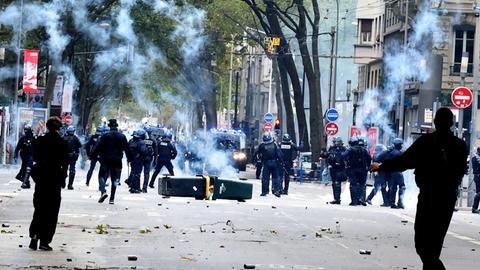 Lyon, Frankreich: Auf einer Straße stehen sich Polizeikräfte und Protestler gegenüber. Dazwischen liegen umgefallene Mülltonnen, Qualm ist in der Luft.