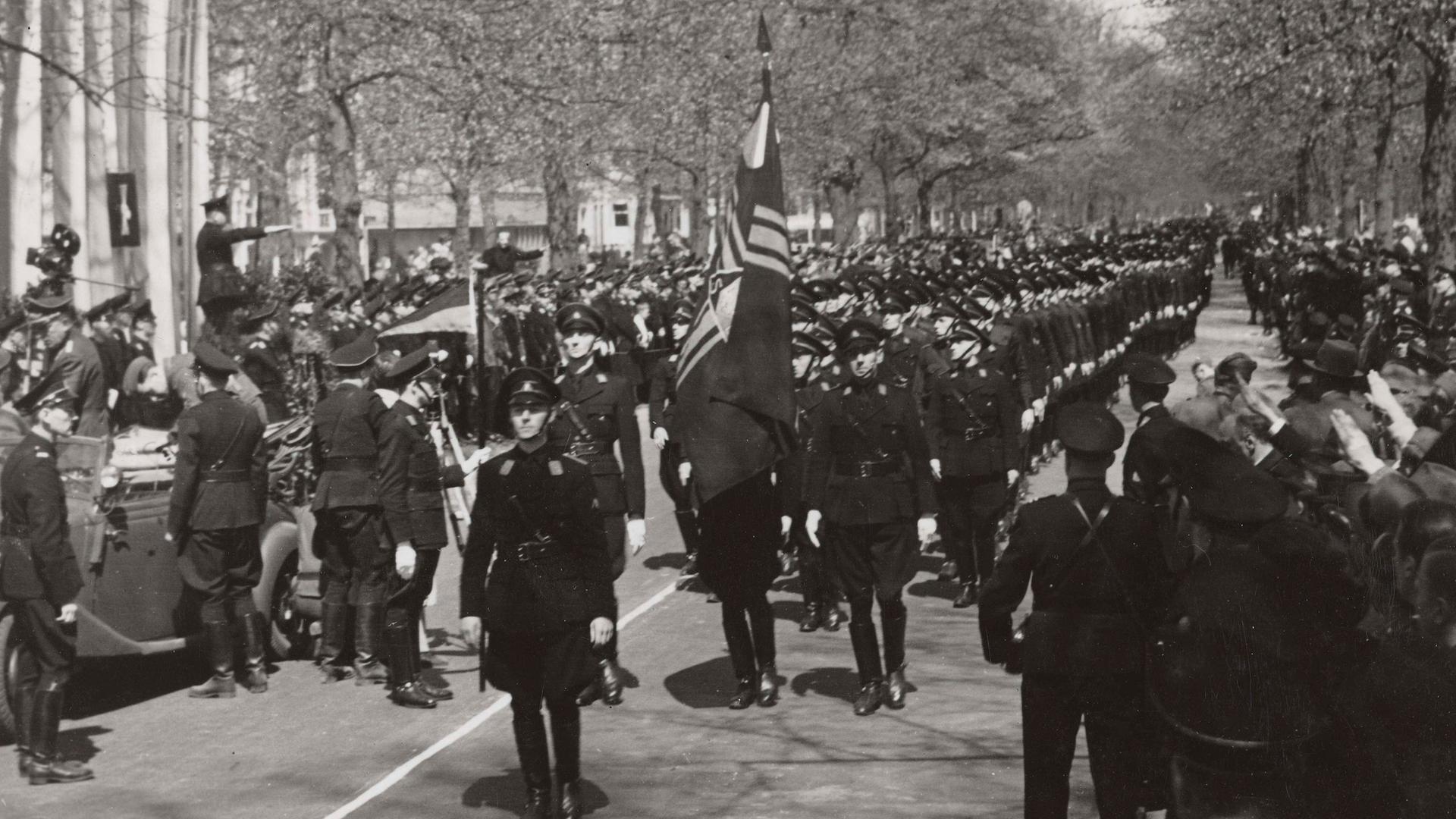 Nationaal-Socialistische Beweging (NSB), faschistische, später nationalsozialistische Partei in den Niederlanden, aktiv 1931 bis 1945 bei einer Parade im Jahr 1941. Vorne geht jemand mit einer Fahen. Im Hintergrund sind Bäume zu sehen.