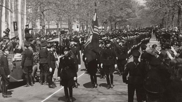 Nationaal-Socialistische Beweging (NSB), faschistische, später nationalsozialistische Partei in den Niederlanden, aktiv 1931 bis 1945 bei einer Parade im Jahr 1941. Vorne geht jemand mit einer Fahen. Im Hintergrund sind Bäume zu sehen.