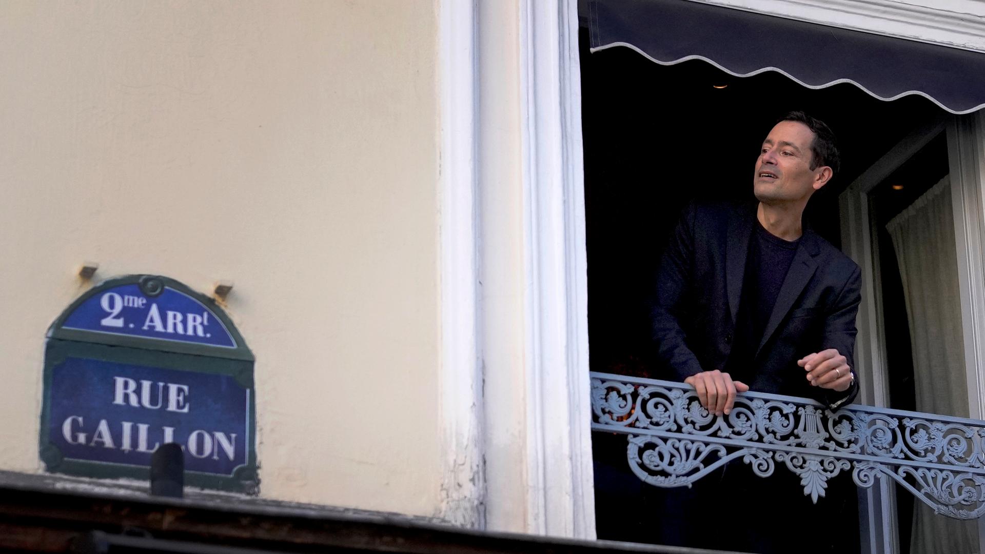 Andrea im schwarzen Jackett lehnt sich lächelnd aus dem Fenster. Auf der Hauswand hängt das Straßenschild "Rue Gaillon". Andrea im schwarzen Jackett lehnt sich lächelnd aus dem Fenster. Auf der Hauswand hängt das Straßenschild "Rue Gaillon".