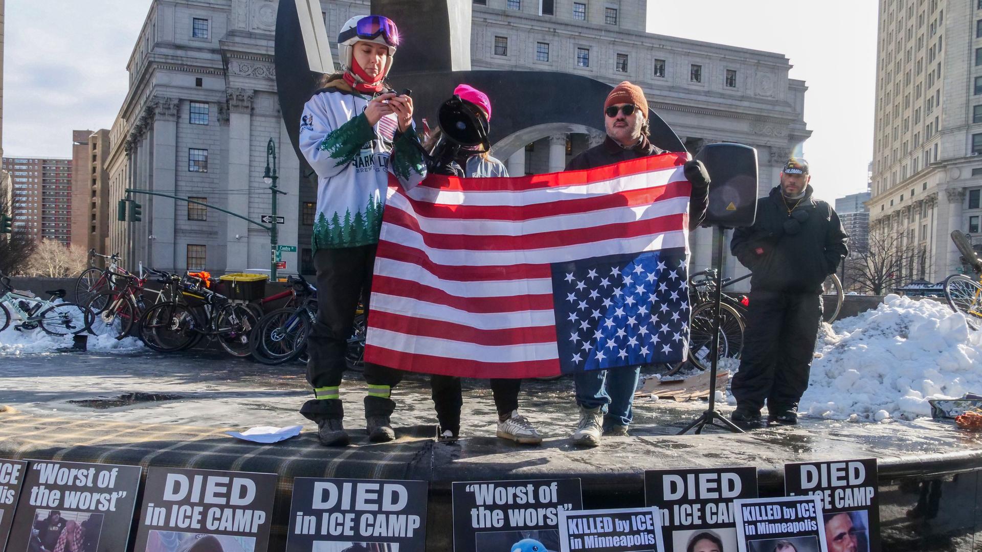 Drei Demonstranten halten die US-Fahne und protesten gegen die gewaltsamen Einsätze der ICE-Agenten Drei Demonstranten halten die US-Fahne und protesten gegen die gewaltsamen Einsätze der ICE-Agenten