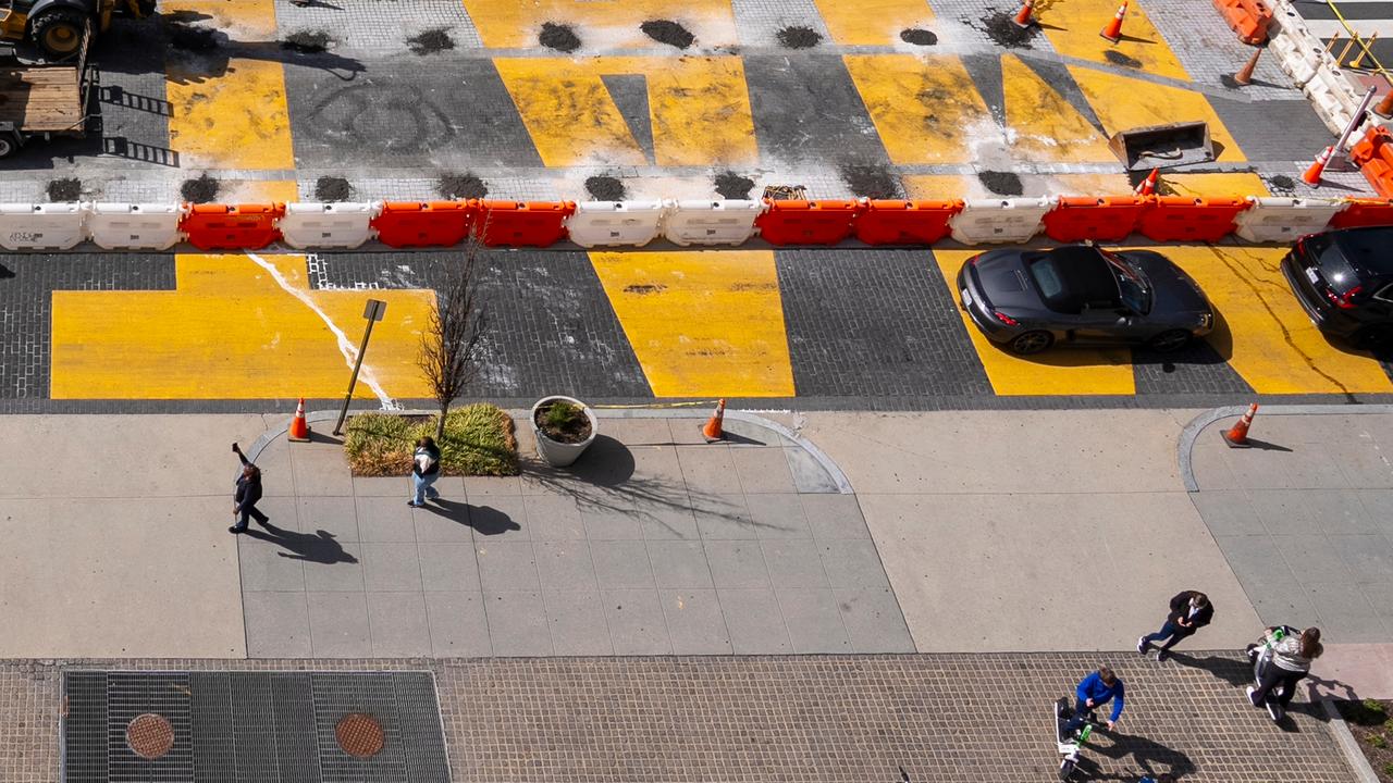 Blick aus der Höhe: In der oberen Bildhälfte sieht man den von rot-weißen Absperrungen gesäumten gelben Schriftzug auf der Straße, der bereits teilweise abgetragen ist. In der unteren Bildhälfte Menschen auf dem Bürgersteig.