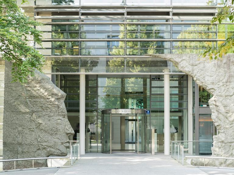Blick auf den Eingang der Max-Planck-Gesellschaft in München, einem Glasgebäude welches am Eingang von zwei Skulpturen umrahmt wird