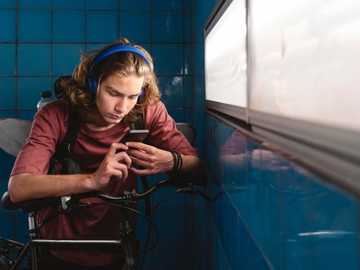 Ein junger Mann mit Kopfhörer und Handy über sein Fahrrad gebeugt. 
