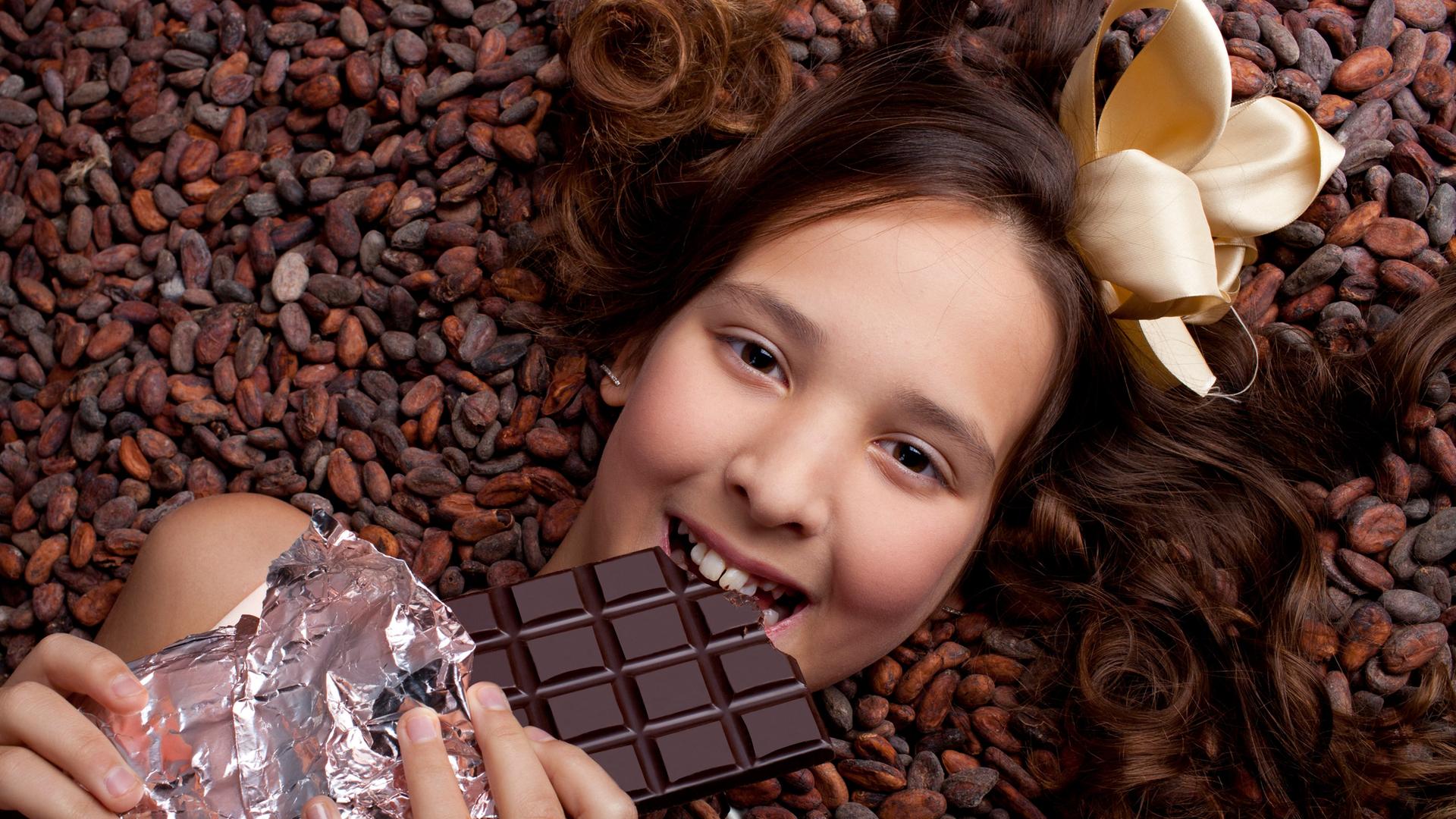 Ein lächelndes Mädchen liegt auf Kakaobohnen und hält eine Tafel Schokolade in der Hand Ein lächelndes Mädchen liegt auf Kakaobohnen und hält eine Tafel Schokolade in der Hand