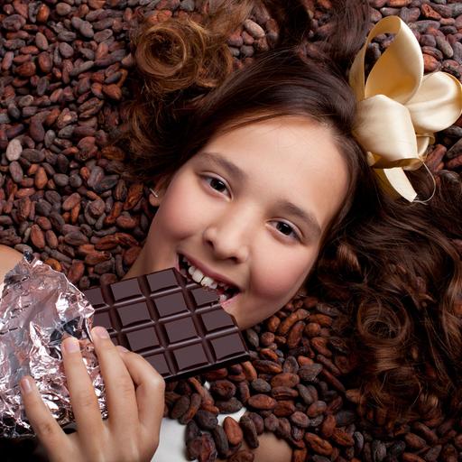 Ein lächelndes Mädchen liegt auf Kakaobohnen und hält eine Tafel Schokolade in der Hand