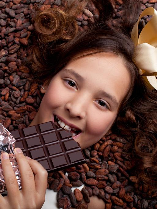 Ein lächelndes Mädchen liegt auf Kakaobohnen und hält eine Tafel Schokolade in der Hand