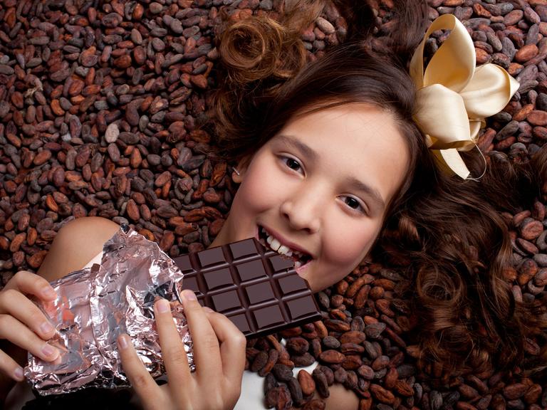 Ein lächelndes Mädchen liegt auf Kakaobohnen und hält eine Tafel Schokolade in der Hand