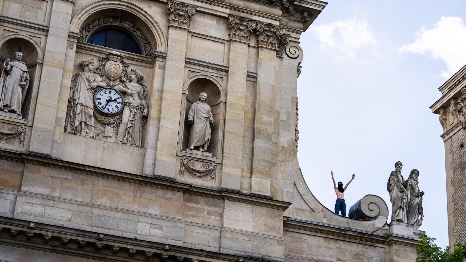 Ein vermummter Demonstrant steht mit erhobenen Armen auf dem Dach der Sorbonne-Universität.