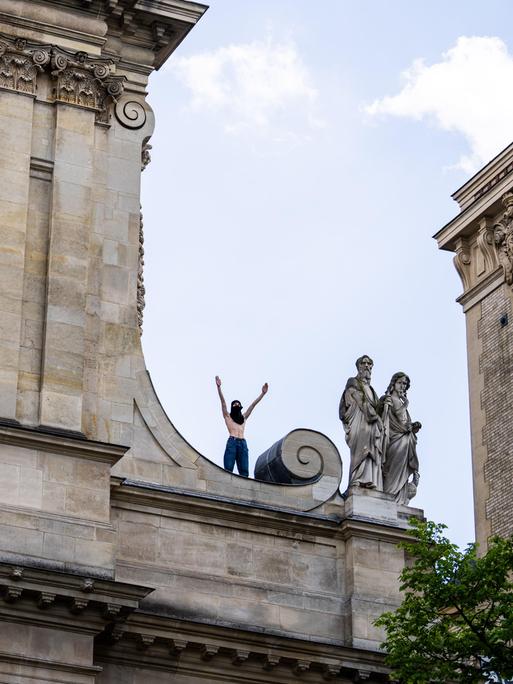 Ein vermummter Demonstrant steht mit erhobenen Armen auf dem Dach der Sorbonne-Universität.