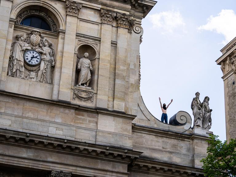 Ein vermummter Demonstrant steht mit erhobenen Armen auf dem Dach der Sorbonne-Universität.