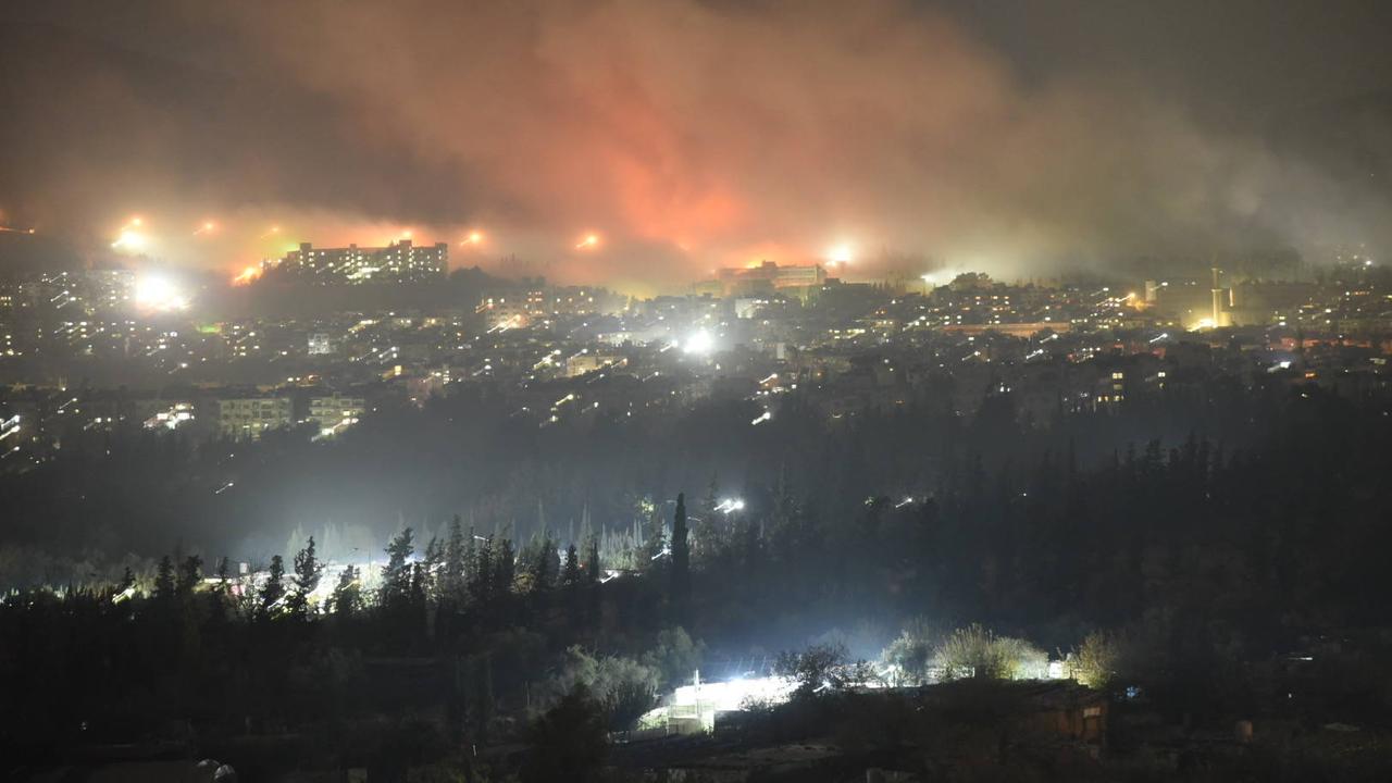 Rauch steigt nachts über Damskus aus. Einschläge, die viele Flammen erzeugen, sind zu sehen.