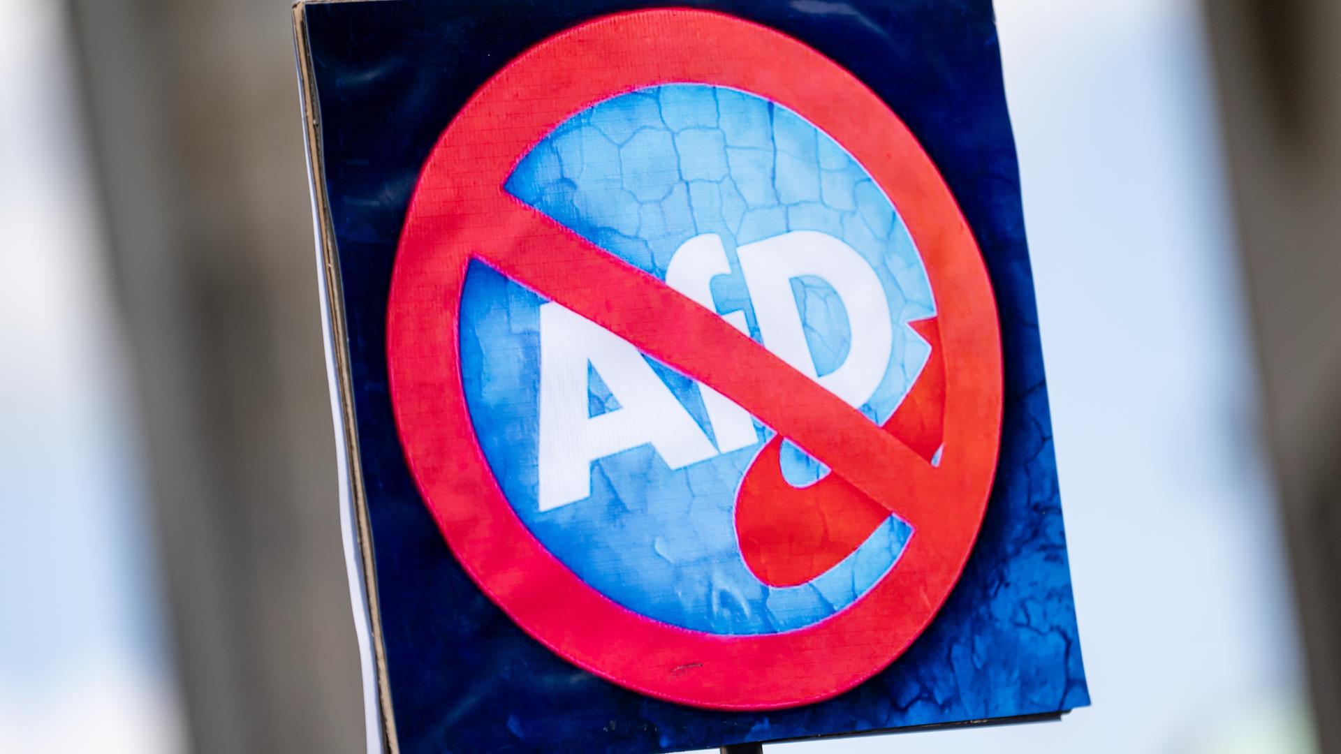 Eine Person hält am bundesweiten Aktionstag "Keine Ausreden mehr - AfD-Verbot jetzt!" am 11. Mai 2025 ein Schild mit einem durchgestrichenen Logo der AfD. 